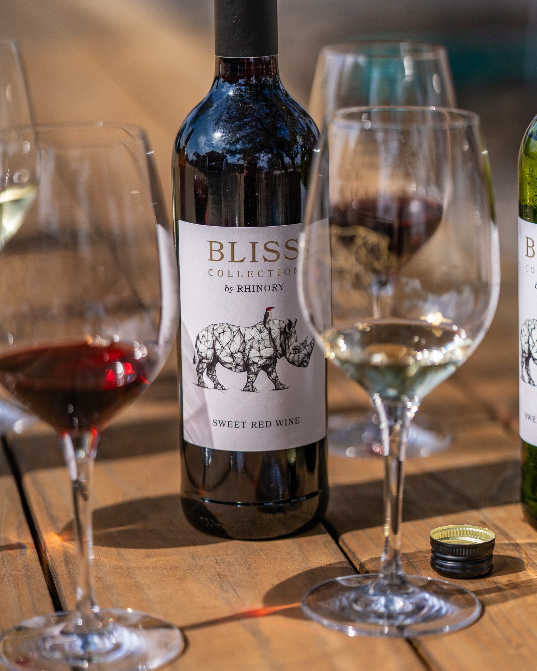 Glasses of red and white beside a bottle on a sunlit wooden table